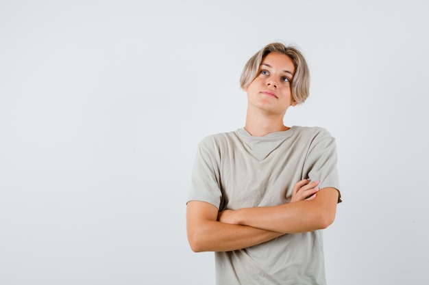 Young teen boy standing with crossed arms, looking up in t-shirt and looking thoughtful. front view.