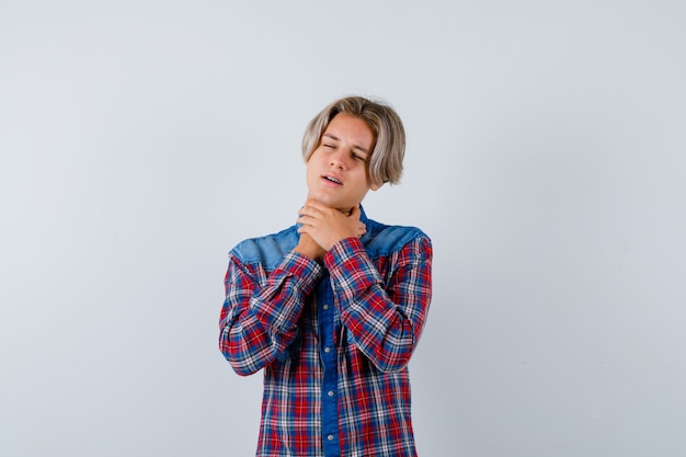 Young teen boy suffering from sore throat in checked shirt and looking bothered , front view.