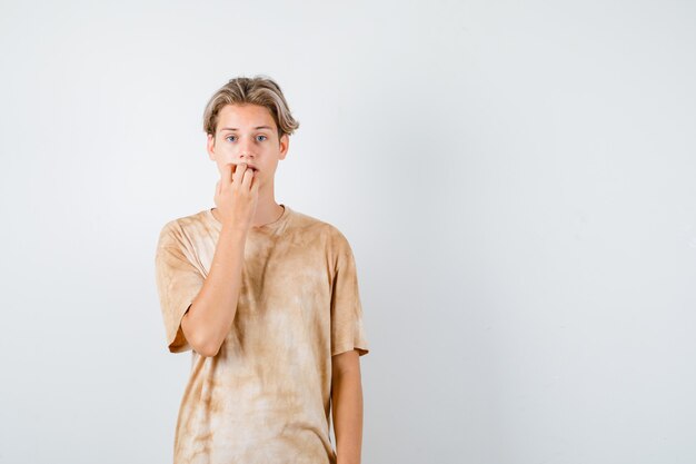 Young teen boy in t-shirt biting nails emotionally and looking anxious , front view.