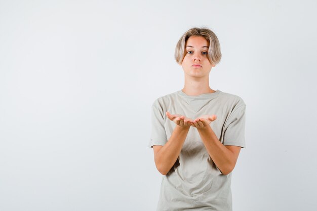 Young teen boy in t-shirt making giving or receiving gesture and looking focused