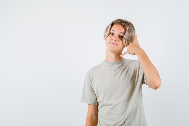 Young teen boy in t-shirt showing phone gesture and looking cheery , front view.