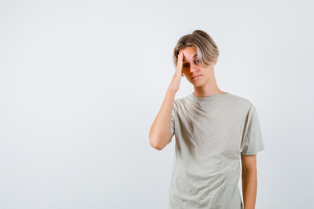 Молодой мальчик-подросток в футболке страдает от головной боли и выглядит усталым