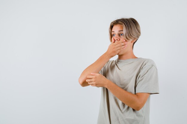 Young teen boy in t-shirt with hand on mouth