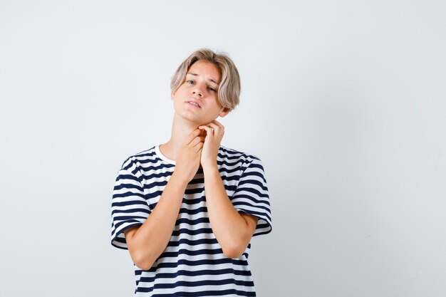 Young teen boy touching neck with hands in striped t-shirt and looking distressed. front view.