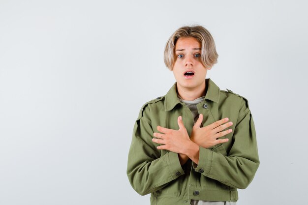 Young teen boy with crossed hands on chest in green jacket and looking scared