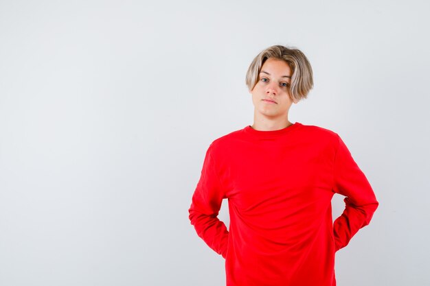 Young teen boy with hands behind back in red sweater and looking pensive , front view.