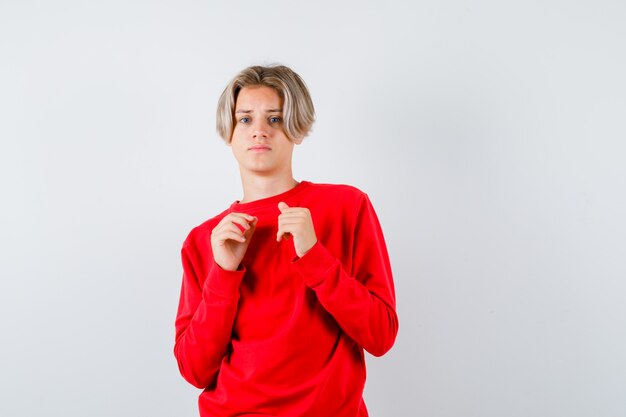 Young teen boy with hands over chest in red sweater and looking scared. front view.