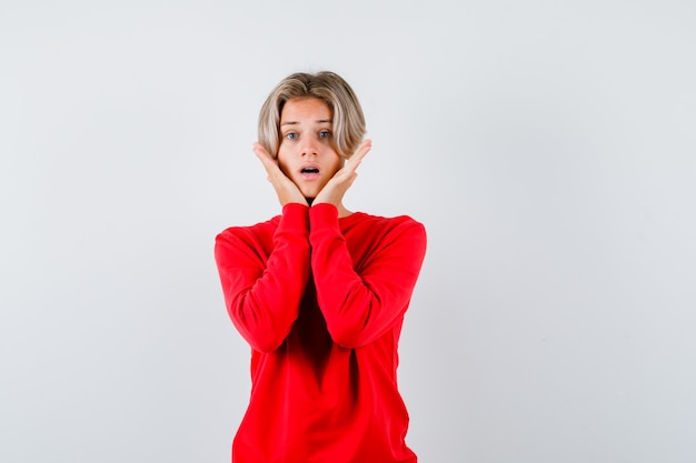 Young teen boy with hands under chin in red sweater and looking anxious. front view.