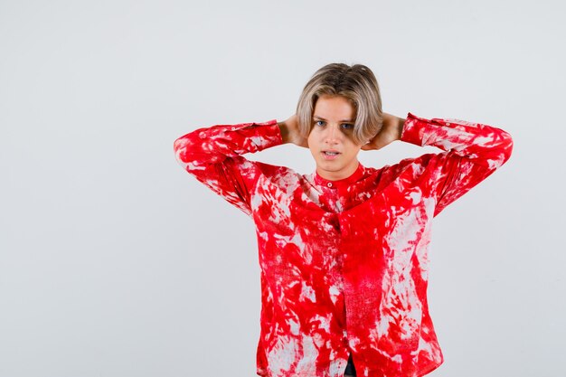 Young teen boy with hands behind head in shirt and looking serious. front view.