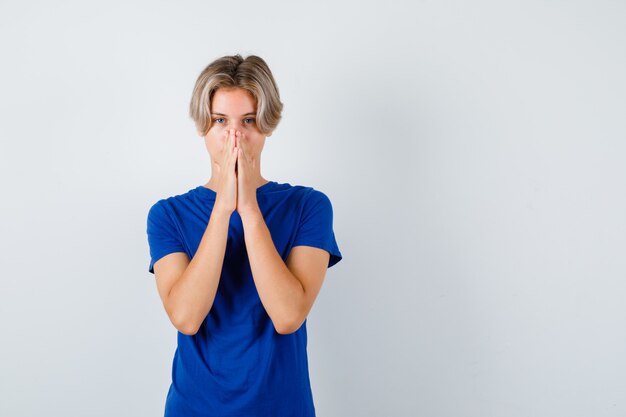 Молодой мальчик-подросток с руками в молитвенном жесте в синей футболке и обнадеживающим взглядом. передний план.
