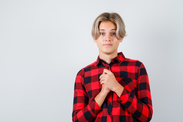 Young teen boy with hands in praying gesture in checked shirt and looking hopeful. front view.