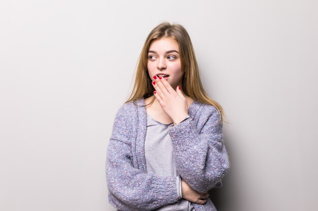 Young teen girl covers her mouth in shock hand on a gray wall