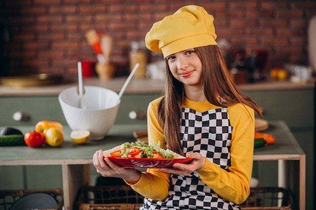 Young teen girl preparing salad for breakfast at the kitchen