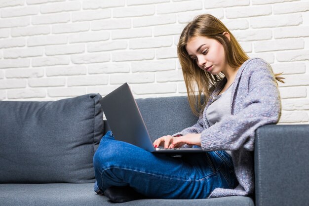 自宅のベッドルームに座って、ラップトップに取り組んで、手紙を書いて、自宅でインターネットを閲覧する若い十代の少女