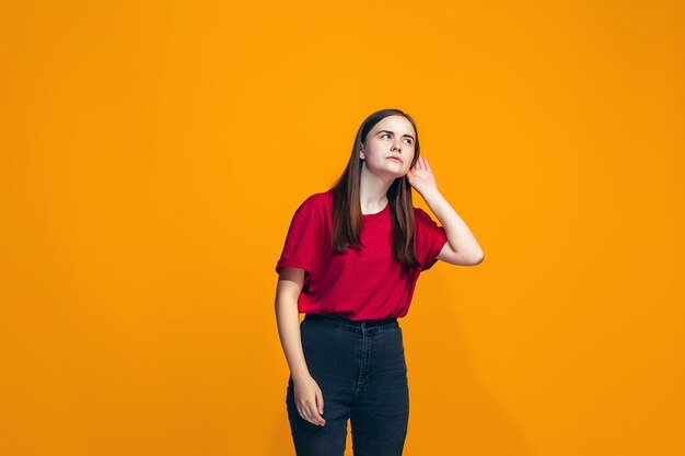 The young teen girl whispering a secret behind her hand over orange background