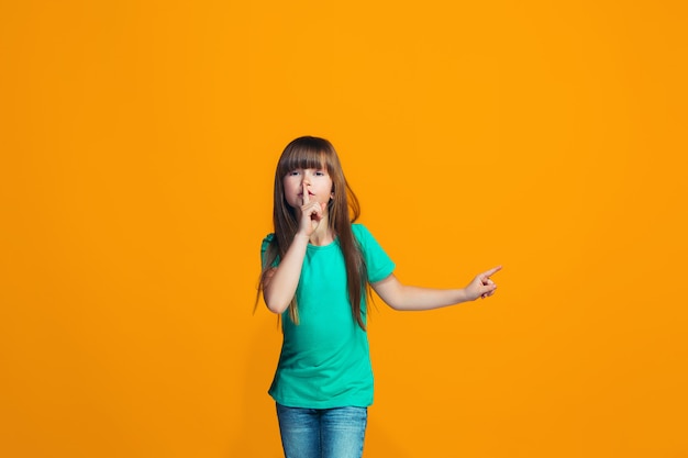 The young teen girl whispering a secret behind her hand over orange space