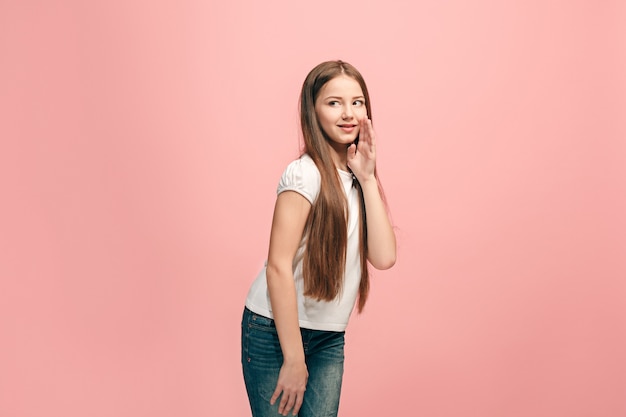Молодая девушка шепчет секрет за рукой над розовой стеной