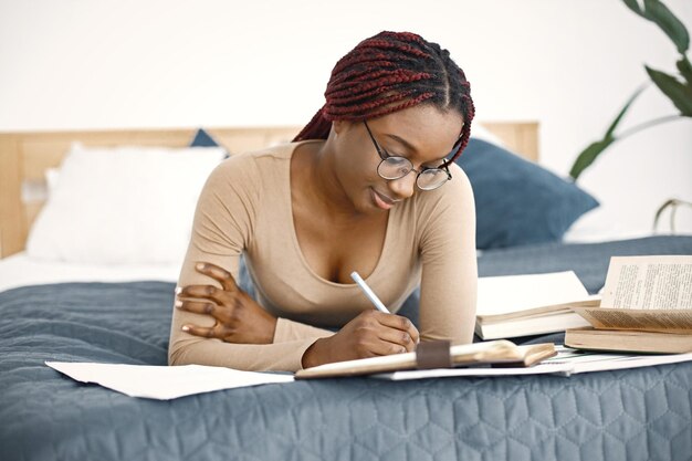 Young teenage girl lying on her bed studying in light bedroom at home