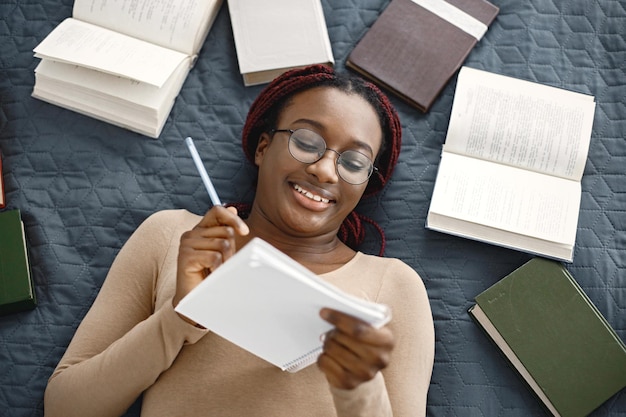 Young teenage girl lying on her bed studying in light bedroom at home