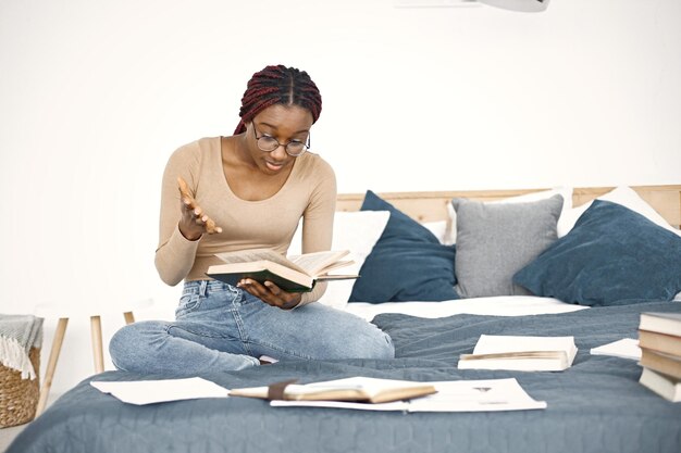 Young teenage girl sitting on her bed studying in light bedroom at home