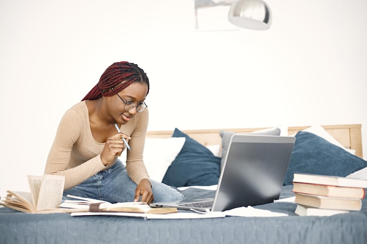 Free Photo young teenage girl sitting on her bed studying and using a laptop