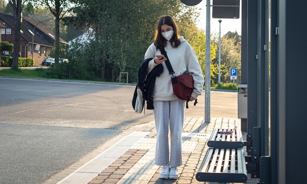 A young teenage woman is waiting for a bus at a bus stop early in the morning