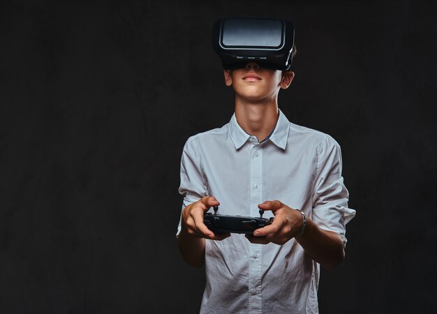 Young teenager dressed in a white shirt wears virtual reality glasses and controls the quadcopter using the control remote.