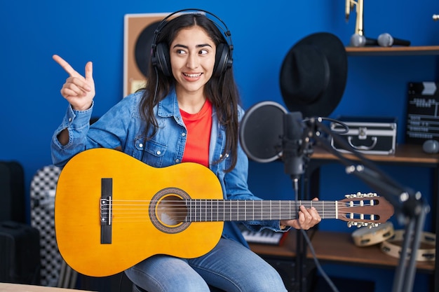 無料写真 音楽スタジオでクラシック ギターを弾く若い 10 代の女の子が口を開けて幸せな笑みを浮かべて横に親指を指す