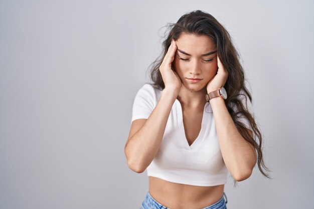 Young teenager girl standing over white background with hand on head, headache because stress. suffering migraine.