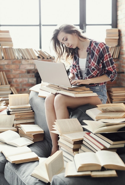 Young teenager girl using the laptop computer surrounded by many books.
