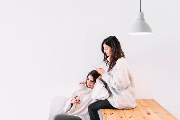 Young tender girlfriends with phones in kitchen