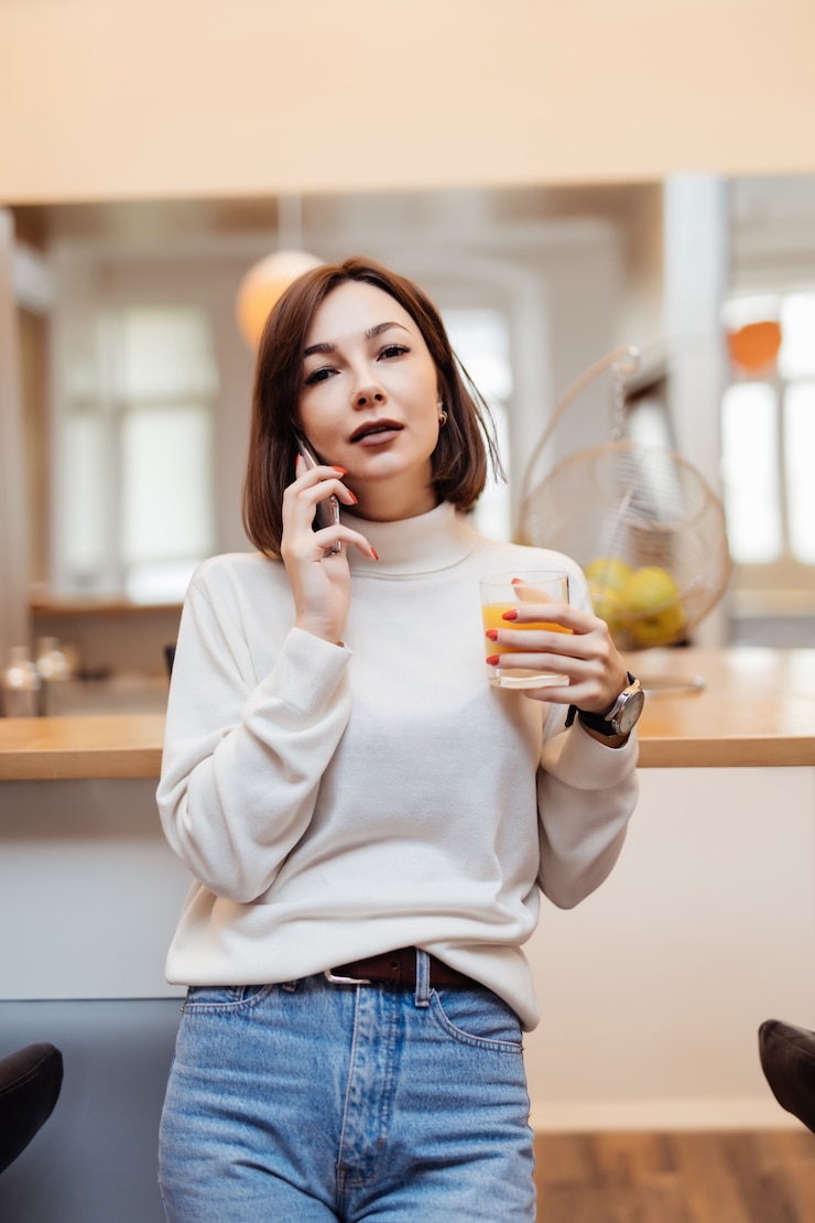無料Photo 若い柔らかい女性が電話で話しているキッチンにいます。