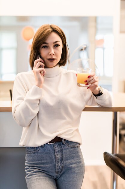 Young tender lady in white t-shirt and blue jeans in the kitchen talking on the phone