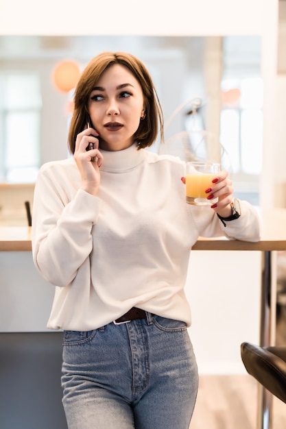 Young tender lady in white t-shirt and blue jeans in the kitchen talking on the phone