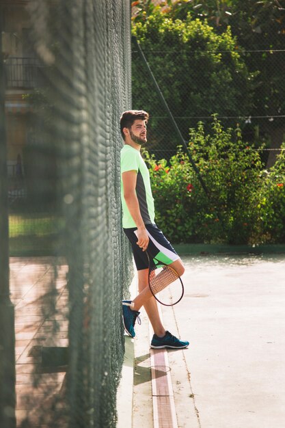 Young tennis player leaning against fence