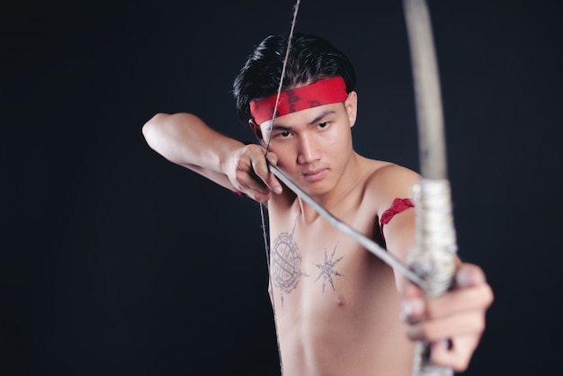 young THAILAND male warrior posing in a fighting stance with a bow