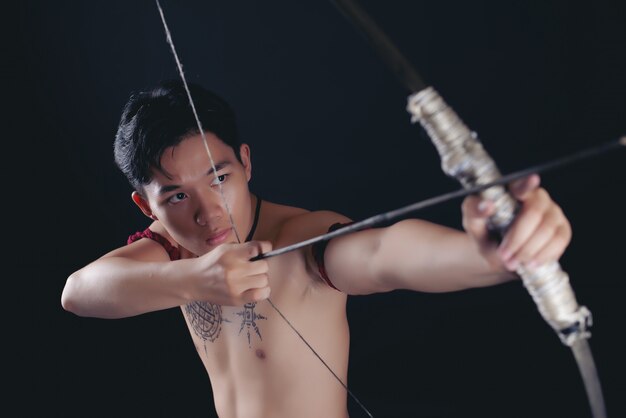 young THAILAND male warrior posing in a fighting stance with a bow