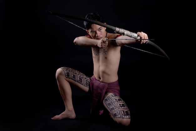 young THAILAND male warrior posing in a fighting stance with a bow