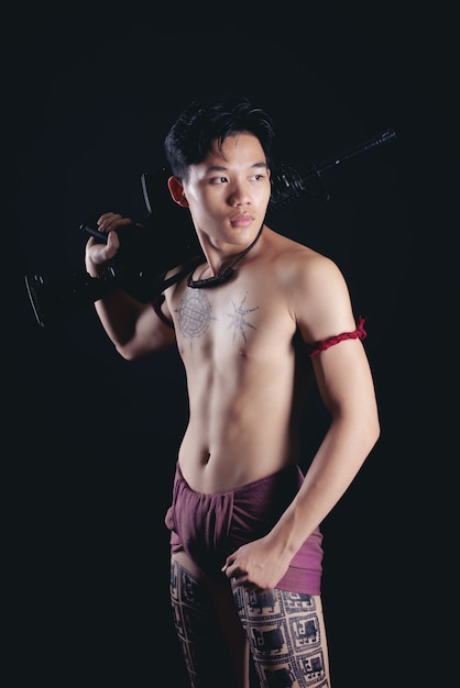 young THAILAND male warrior posing in a fighting stance with a firearm