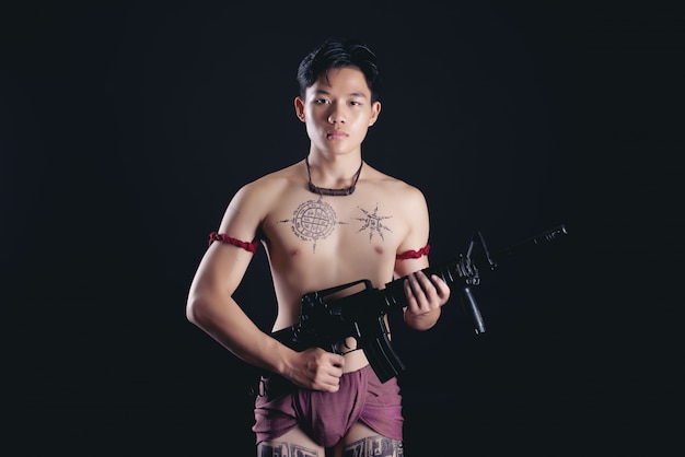 young THAILAND male warrior posing in a fighting stance with a firearm