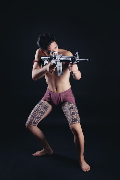 Free photo young thailand male warrior posing in a fighting stance with a firearm