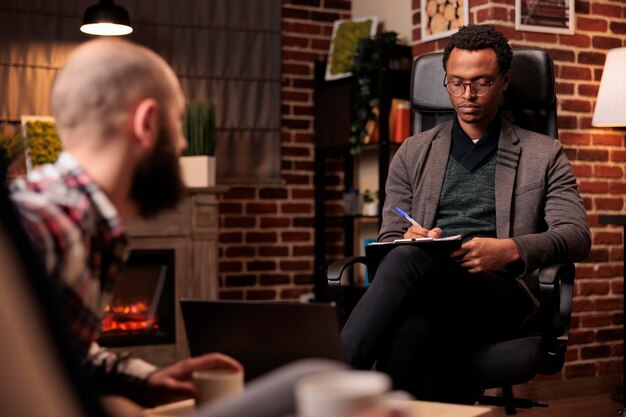 Young therapist taking notes on paper at psychotherapy session with couple arguing on couch. Writing marriage problems to find solution and solve conflict, giving professional counseling advice.