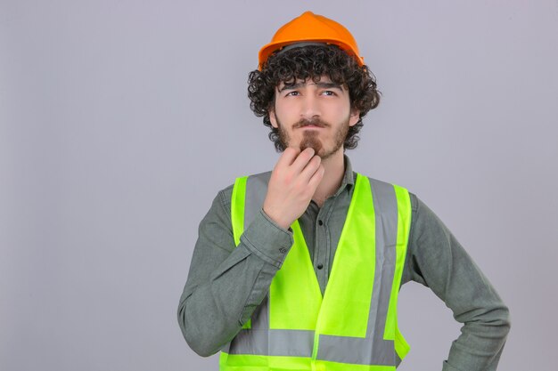 Young thoughtful breaded handsome engineer worker standing with puzzled look scratching chin thinking over isolated white background