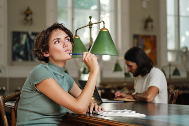 Young thoughtful female student thinking about new study project in library of university