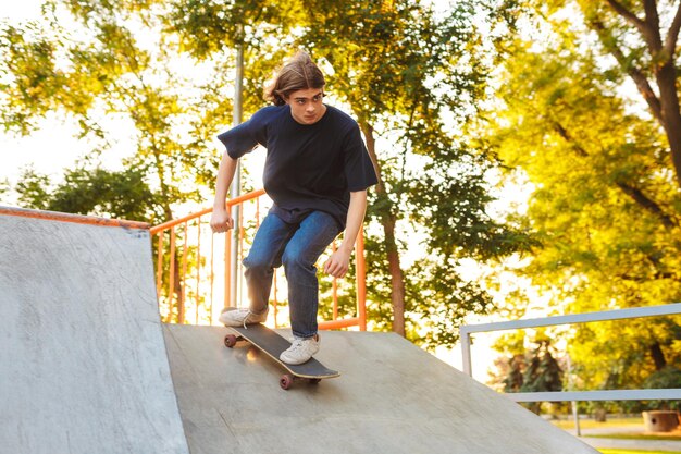 Young thoughtful skater practicing tricks with skateboard on springboard at modern skate park