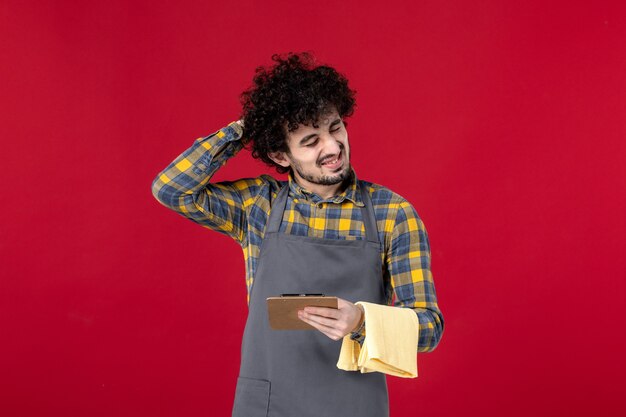 young tired male server with curly hair holding towel taking order on isolated red background