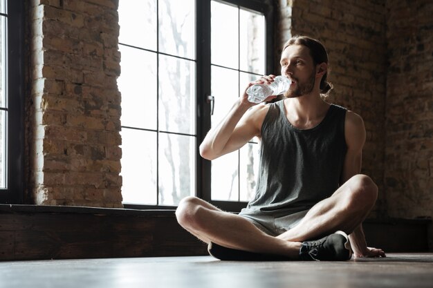 Young tired sportsman sitting on the floor