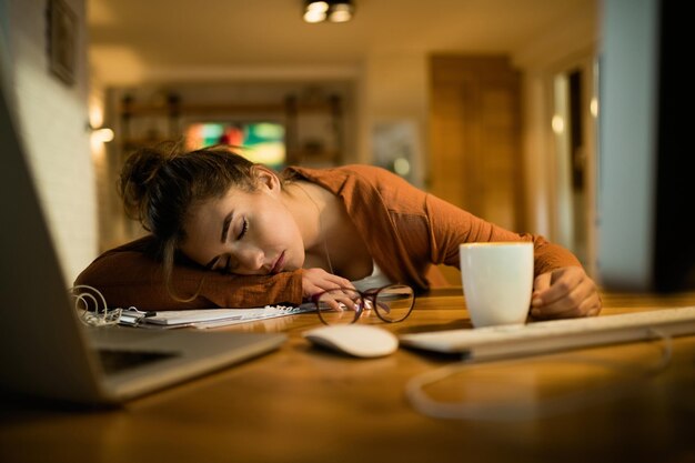 Young tired woman napping at her desk while working late at night at home