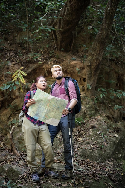 Young tourist couple traveling on holidays in forest looking at map in search of attractions. Travel concept.