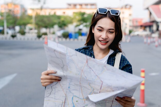 紙の地図を持ってチェックしている若い観光客の女性、彼女は幸せそうに見て笑顔